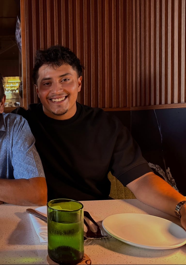 Man smiling at dining table with green glass and white plate, brown paneled wall background